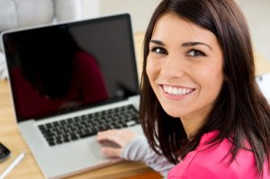 a person sitting at a desk with a laptop and smiling at the camera