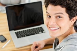 a young man smiling while using a laptop