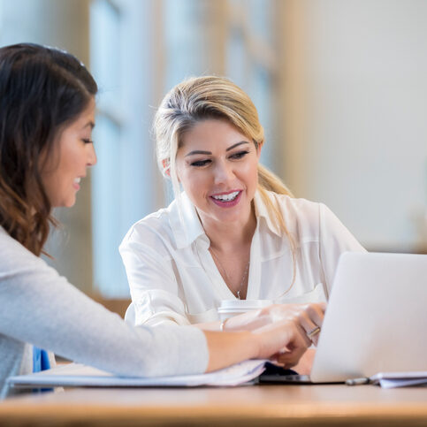 Confident female college students study together for exam Diverse female college students review something on a laptop while studying for an exam.